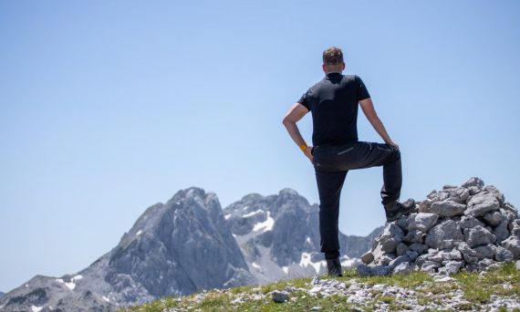 A hiker stands atop a rocky peak, enjoying a breathtaking mountain view on a clear day.